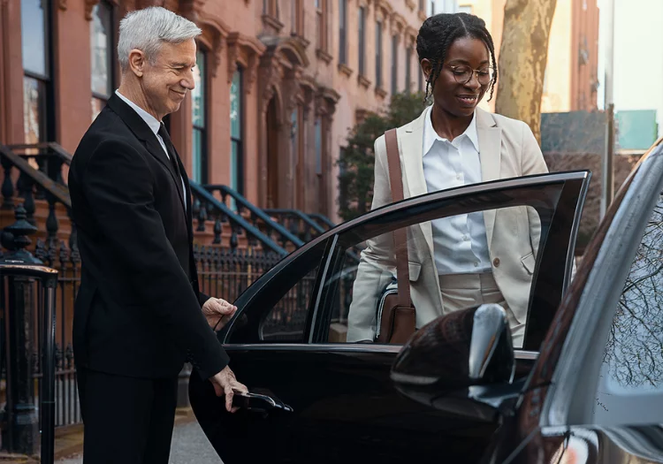 A chauffeur in black dress opening the door of a luxury black sedan for a passenger